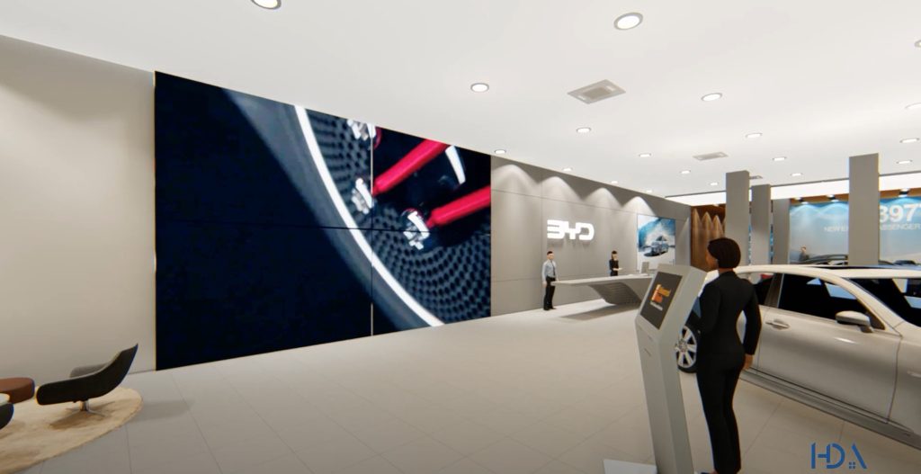 BYD showroom Dhaka main floor interior — full-size white BYD electric vehicle on display, large LED video wall with car close-up, BYD logo on curved grey reception desk, digital kiosk stand, uniformed sales staff, warm tile floor and timber accent columns, House De Arch Bangladesh