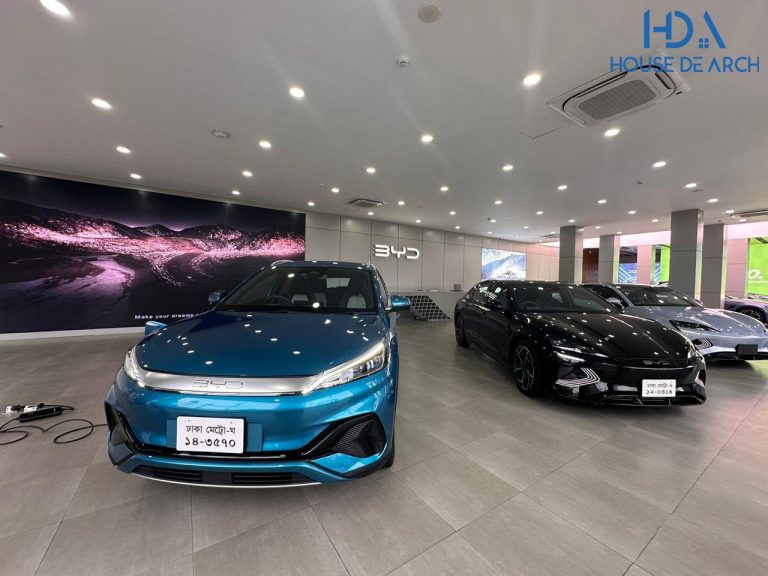Blue BYD electric sedan on the showroom floor of the BYD flagship showroom in Tejgaon, Dhaka, with an EV charging cable and further vehicles visible behind it